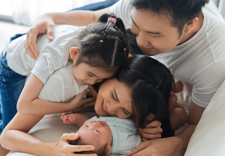 Mom, dad, daughter snuggling a newborn baby